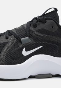 Nike trainingsschoen met een zwarte mesh bovenkant, witte tussenzool en een zilveren logo. Geverfde oppervlakken en vetersysteem voor een veilige pasvorm.