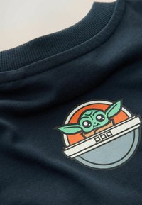Navy blue cotton T-shirt featuring a circular graphic of a character with large ears, set against orange and gray accents.