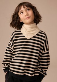Maglione a righe nere e avorio con vestibilità oversize e polsini a coste. Sciarpa cremoso morbida e testurizzata disposta attorno al collo.