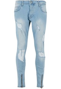 Világoskék farmer skinny farmernadrág, amely elhasználódott szakadásokat és rojtos éleket tartalmaz. Cipzár részletek találhatók a bokáknál. Klasszikus öt zsebes kialakítás.