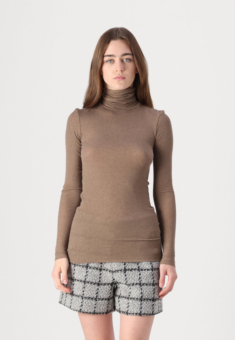 Brauner, gerippter Rollkragenpullover mit langen Ärmeln; kombiniert mit grauen Karoshorts aus strukturiertem Stoff und taillierter Passform.