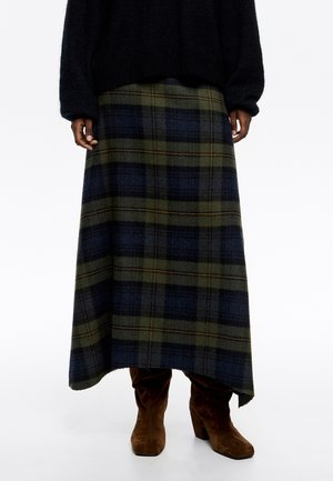 Falda maxi de cuadros en tonos verde oscuro, azul marino y marrón, confeccionada en suave lana, con un diseño fluidos y un dobladillo ligeramente deshilachado. Botas de ante marrón.