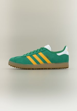 Πράσινο αθλητικό παπούτσι Adidas Gazelle με κίτρινες ρίγες, λευκή φτέρνα, καουτσούκ σόλα και ταιριαστά πράσινα κορδόνια, εμφανιζόμενο από το πλάι σε ουδέτερο φόντο.