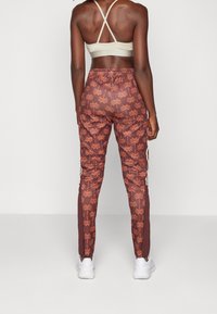 Bruna mönstrade träningsbyxor med palmträdsmotiv, elastisk midja och vita sidostrecker, matchade med en ljusbeige sportbehå.