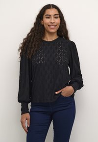 Černý top s dlouhým rukávem, zdobený texturovanými diamantovými vzory, kulatým výstřihem a nabráním na rukávech, v kombinaci s tmavomodrýmiúzkými džínami.