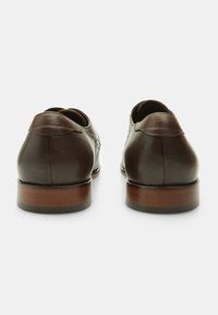 Scarpe in pelle marrone con finitura liscia, punta tonda e cuciture decorative. Tacco piatto con dettagli in legno e design elegante.