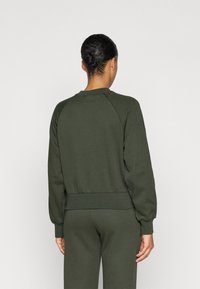 Zöld pulóver kerek nyakkivágással, raglán ujjal és szűkített derékrésszel. Puha anyagból készült, sima textúrával.