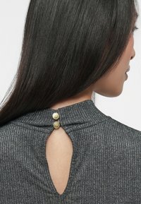 Grå tekstureret top med en nøglehulskæring i ryggen og to guldknapper ved halsudskæringen. Stoffet har en subtil glans.