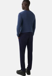 Men's outfit featuring a long-sleeve navy sweater and dark navy trousers, paired with black shoes and sunglasses. Smooth fabric texture.