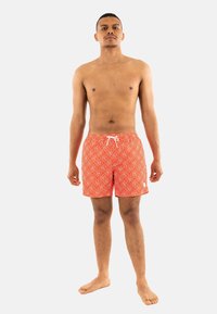 Pantaloni da bagno rossi con un motivo geometrico bianco, vita elasticizzata e cordino. Tessuto morbido con lunghezza a metà coscia e senza tasche.