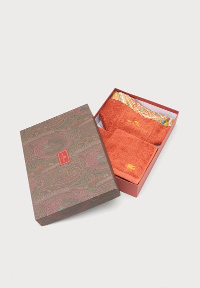 Boîte décorative ouverte avec motif cachemire contenant des serviettes pliées orange brûlé, dont une avec un bord multicolore et une broderie dorée.