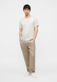 Ανοιχτό γκρι κοντομάνικο μπλουζάκι, φαρδιά μπεζ λινά παντελόνια και λευκά αθλητικά παπούτσια. Το ύφασμα είναι λείο με ήπια υφή.