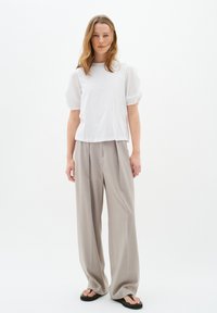 Haut blanc à manches courtes avec des manches bouffantes, associé à un pantalon large beige taille haute et des tongs noires. Design minimaliste, tissu lisse.