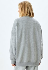 Hellgrau oversized Sweatshirt mit geripptem Kragen und Ärmelbündchen, das eine glatte, weiche Textur und gesenkte Schulternaht hat.