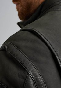 Giacca in pelle nera con cuciture in evidenza, superficie testurizzata e design strutturato delle spalle. Ingrandimento dell'area delle spalle e del colletto.