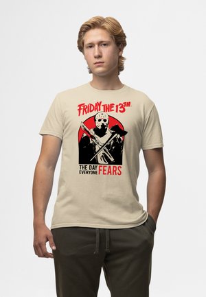 Béžové bavlněné tričko s potiskem zobrazujícím postavu v masce s překříženými zbraněmi, obklopenou červeným kruhem a černým textem.