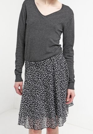 Kvinde iført en mørkegrå langærmet V-hals sweater og en sort nederdel med hvide polkaprikker.
