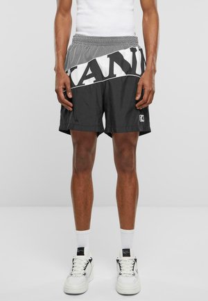 Sorte shorts med et hvidt og sort grafisk bånd, med en elastisk talje og en glat stofstruktur. Hvide sneakers fuldender looket.
