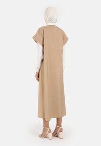 Beige dlouhé šaty s krátkými rukávy, jemná textura a volný střih. Doplněné o světlé sandály, které ladí s minimalistickým designem.