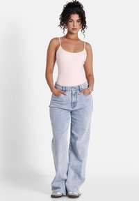 Ljusrosa bodysuit med tunna axelband och en logotyp. Ljusblå vida jeans med framfickor och hög midja.