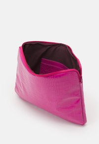 Vaaleanpunainen krokotiilinkuosiset kosmetiikkalaukku, jonka vetoketju on osittain auki, paljastaen tyhjät tummat sisätilat ja pienen sisätaskun.