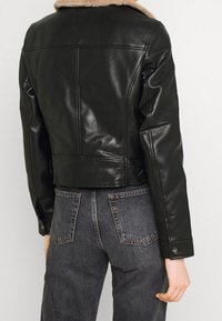 Zwarte leren jas met een kraag van imitatiebont, cropped ontwerp en een gladde textuur. Heeft knoopmanchetten en een detail van een naad aan de achterkant.