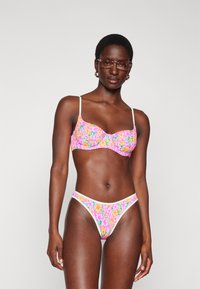 Blumen-Bikini-Set mit einem Muster aus Pink, Lila und Gelb. Der Bh hat weiche Cups und dünne Träger; der passende String hat einen weißen Saum.