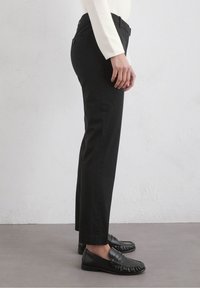 Black trousers with a slim fit, flat front, and belt loops. Paired with black loafers, showcasing smooth leather texture.
