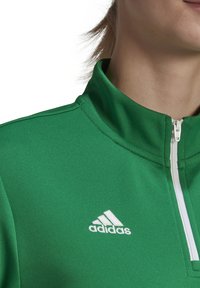 Groene sportieve zip-up jas met een gestructureerd oppervlak, voorzien van een witte Adidas-logo op de borst en een rechte kraag.