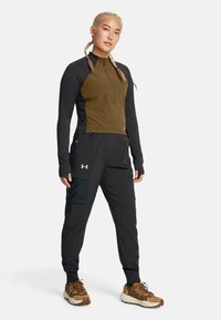 Conjunto atlético que incluye una chaqueta con cremallera en tonos marrones y negros, pantalones negros con un bolsillo lateral y zapatillas de senderismo marrones. Texturas suaves, diseño práctico.