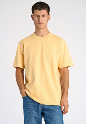 Camiseta de algodón de manga corta y cuello redondo en color amarillo claro. Presenta un corte relajado, una textura suave y un diseño liso sin patrones ni acentos.