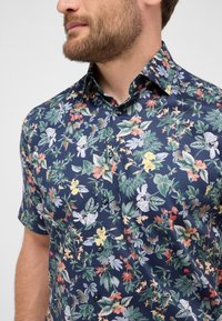 Korte mouw shirt van marineblauwe stof met een levendig bloemenpatroon met veelkleurige bloemen en groene bladeren; inclusief zwarte knopen.