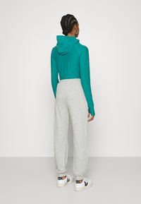 Hoodie azul-petróleo com um bolso nas costas e calças de moletom cinzentas, com punhos elásticos e cintura com cordão, combinadas com sapatilhas brancas.