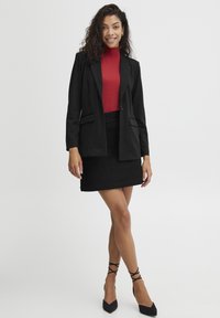 Černý blazer s klopami, kombinovaný s přiléhavým červeným rolákem a černou mini sukní. Úzký design s špičatými černými podpatky a křížovými popruhy.