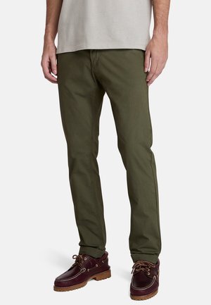 Olive green chinos with a straight fit, made from cotton. Features standard pockets and a smooth texture; paired with dark brown boat shoes.