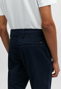 Navy cotton trousers with a smooth texture, featuring a fitted design, belt loops, and two back pockets. Logo tag visible at the waistband.