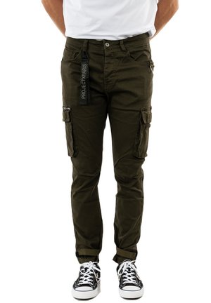 Olivengroene cargobroek met meerdere zijvakken, verstelbare manchetten en een labeltag. Gecombineerd met zwart-witte sneakers.