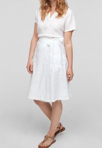 Witte linnen wikkelrok met een strik taille, voorzien van twee zijzakken en een knielange zoom, gecombineerd met een lichtgewicht witte top.