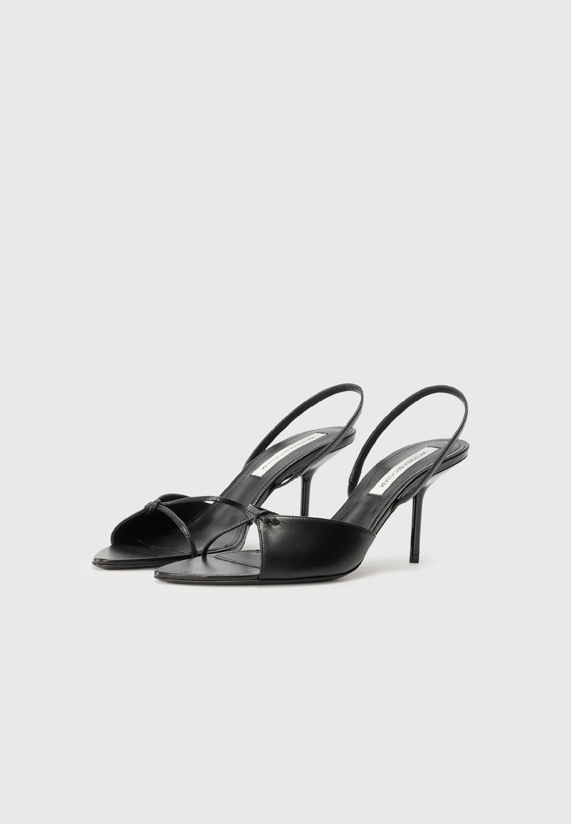 Des escarpins à talons slingback en cuir noir avec un bout pointu, un detail noué à l'avant et un talon stiletto fin. Texture lisse et design minimaliste.