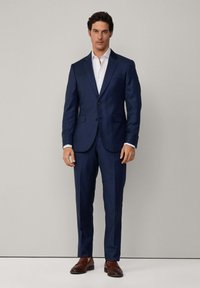 Costume bleu marine à la coupe ajustée, doté d'une fermeture à deux boutons, de revers crantés et de poches latérales. Assorti à une chemise blanche et des chaussures marron.