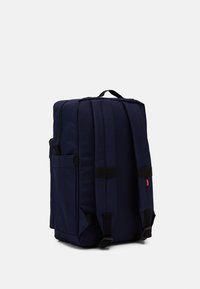 Navy blue backpack with a rectangular shape, fabric material, padded shoulder straps, and zipper closure, featuring side pockets and logo detail.