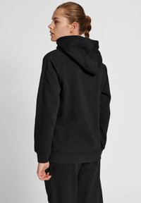 Svart hoodie av mjukt material med huva, ribbade ärmslut och kenguruficka. Har en avslappnad passform och minimalistisk design.