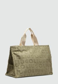 Oliwkowa torba tote z płótna o teksturowanej powierzchni, z wytłoczonym logo, dwiema kremowymi rączkami oraz zorganizowanym kształtem.
