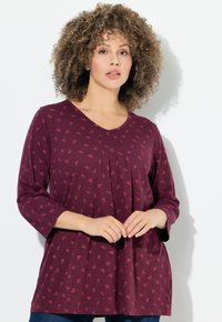 Top color bordeaux con maniche a tre quarti, scollo a V e pieghe frontali. Presenta un motivo sottile ed è realizzato in tessuto morbido.
