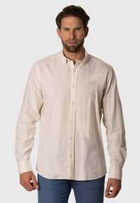 Camisa de manga larga, con botones, en beige claro, hecha de un tejido texturizado. Presenta un clásico cuello y un sutil logo bordado en el pecho.