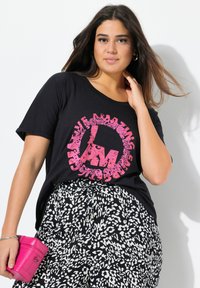 Černé tričko s krátkým rukávem s růžovým kulatým nápisem. Kombinováno s kalhotami s černobílým vzorem. Drží malou růžovou tašku.