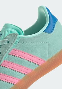 Světlé modré semišové tenisky s růžovými cikcak pruhy, modrými akcenty na patě a průhlednou gumovou podrážkou. Texturovaný povrch.