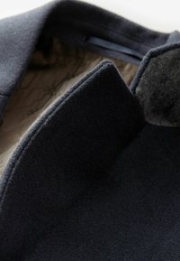 Collar de abrigo de lana en azul marino oscuro con un interior texturizado, presentando un acabado suave y costuras limpias a lo largo de los bordes.