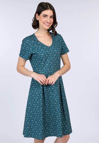 Tefarbendes Kleid aus weichem Stoff mit kurzen Ärmeln und V-Ausschnitt. Es hat ein Blumenmuster mit kleinen weißen und gelben Blumen. Ausgestellte Silhouette.