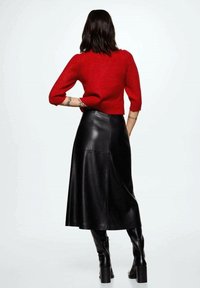 Un pull en tricot rouge à manches courtes associé à une jupe midi en cuir noir et des bottes noires jusqu'aux genoux, mettant en valeur une silhouette ajustée.